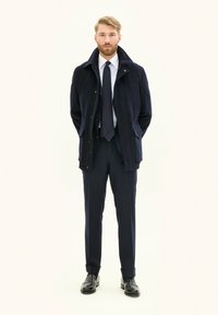 Laivan sininen trench coat yli valkoisen paidan ja laivan siniset raidoitetut housut. Mustat nahkakengät, joissa on kapea istuvuus ja yksityiskohtainen ompelu koko matkalta.