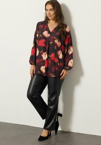 Top nero fluido con stampa floreale rossa e crema, abbinato a pantaloni in ecopelle neri e scarpe con tacco nere.