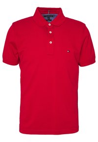 Polo rouge avec patte de boutonnage, manches courtes et tissu texturé. Présente un petit logo multicolore sur la poitrine gauche.