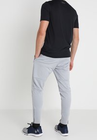 Graue sportliche Jogginghosen mit schmalem Schnitt, elastischem Bund, seitlichen Taschen und Reißverschlüssen an den Knöcheln, kombiniert mit einem schwarzen Kurzarmshirt.