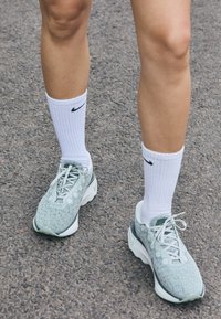 Svetlozelené športové topánky s textúrovaným sieťovaným zvrškom, kruhovými akcentmi a bielymi šnúrkami, doplnené bielymi, rebrovými ponožkami Nike.