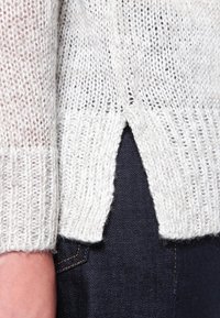 Vaaleanharmaa neulottu neulepaita kuvioidulla pinnalla, jossa on sivuhalkio helmassa ja resorireunat hihoissa.