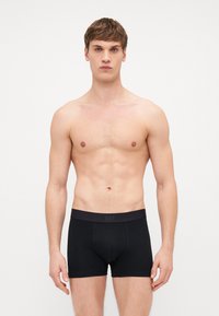 Boxer-briefs noirs en coton, avec une ceinture élastique douce portant le logo "GAP". Texture lisse, design basique et coupe ajustée.