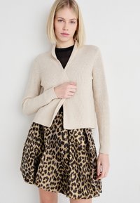 Beige rillede strik cardigan med sjalkrave, parret med en nederdel i guld og sort leopardprint med en flagrende design.