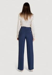 Pantalons navy taille haute avec une coupe droite, dotés de deux poches arrière et de plis subtils à l'avant. Texture de tissu lisse.