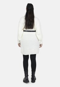 Overdimensioneret hvid strikket sweater med ballonærmer, belagt i taljen med et sort bælte, suppleret med sorte leggings og ankelstøvler.