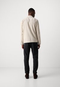 Licht beige corduroyjack met verticale strepen, gecombineerd met donkere spijkerbroek en bruine suède schoenen, gezien vanuit de achterkant. Eenvoudig kraagontwerp.