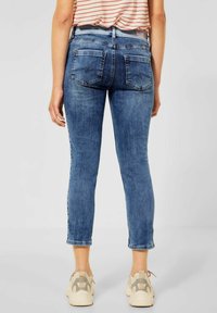 Modré džíny z denimu se slim fit střihem a zkrácenou délkou, se dvěma zadními kapsami a jemným opotřebovaným vzhledem. Spárováno se světlými teniskami.