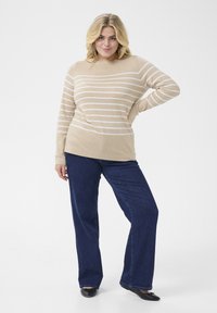 Beige striped sweater with long sleeves and round neckline, paired with dark blue wide-leg jeans and black flat shoes. Clean background.