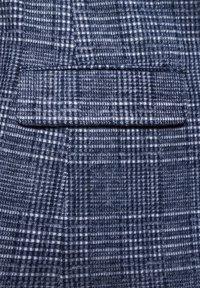 Granatowa tkanina w kratę o miękkiej fakturze; posiada jedną, przeszywaną kieszeń z klapą, eksponującą drobny wzór kraty.