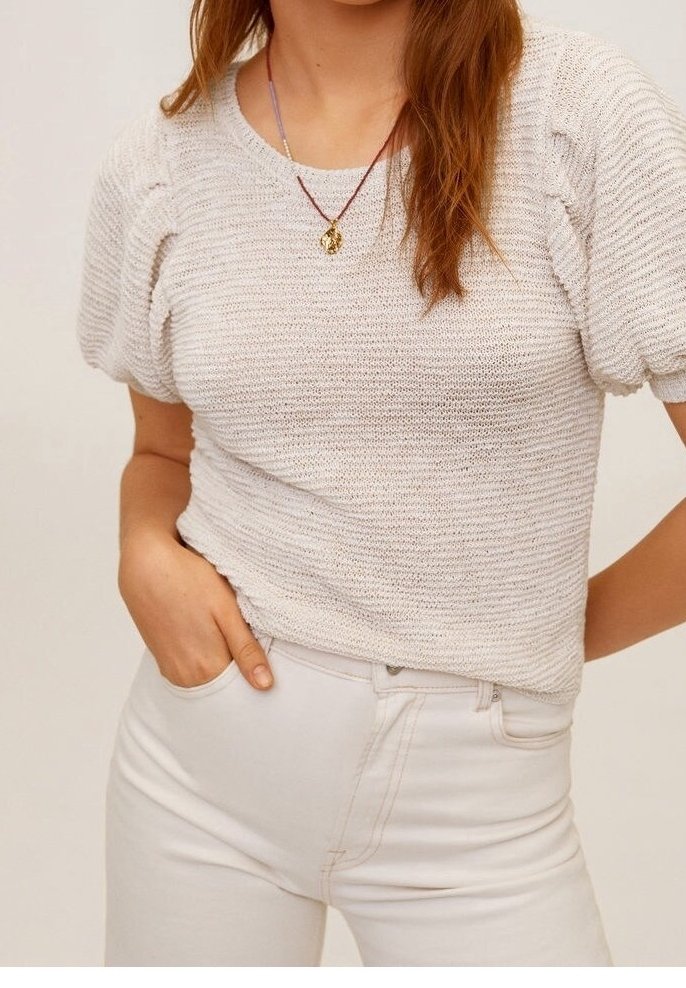 Pull en maille beige clair avec manches courtes bouffantes ; présente un motif côtelé texturé. Associé à un jean blanc ajusté.