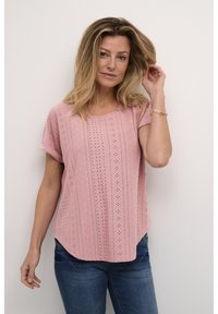 Haut rose à manches courtes avec un motif en œillets et un ourlet arrondi, associé à un jean bleu. Le tissu semble léger et texturé.