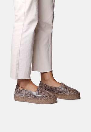 Nohy v leopardích platformových espadrilkách v kombinácii s bielymi skrátenými nohavicami na jednoliatom pozadí.