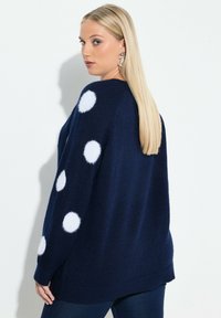 Námořnický modrý oversize svetr s bílými texturovanými tečkami na rukávech, pletená látka, uvolněný střih a boční rozparky. Spodní lem klesá pod boky.