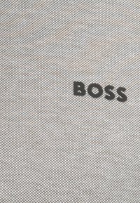 Grauer strukturierter Stoff mit einem Karomuster, auf dem das schwarze, geprägte "BOSS"-Logo deutlich sichtbar ist.