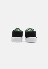 Fekete velúr Vans sneaker, zöld velúr sarokrésszel és fehér gumi talppal. Nincsenek látható minták vagy további fémrészletek.