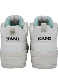 Bele superge iz gladkega usnja in mrežastega materiala. Poudarjene z svetlo modrim notranjim delom in črnim logotipom "KANI" na peti.