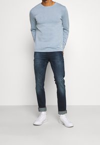 Ljusblå långärmad skjorta med rund hals, tillsammans med mörkblå jeans. Vita sneakers fulländar outfiten. Enkelt design och passform.
