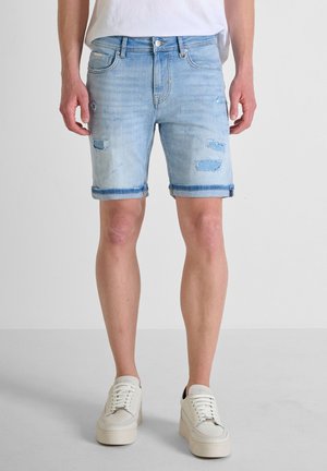 Shorts en denim bleu clair avec des bords effilochés, des détails usés et un ourlet roulé, associés à des baskets crème.
