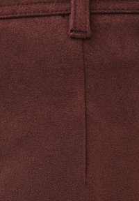 Close-up van bruine suède stof met een centrale naad en een detail van een ceintuurknoop op gestructureerd materiaal.