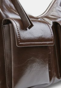 Borsa in pelle marrone con finitura lucida, tasca con pattina frontale e design strutturato. Presenta cuciture pulite e una texture liscia.