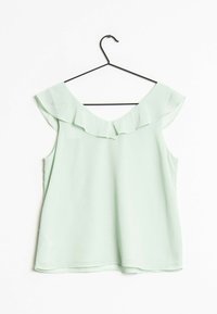 Blusa sin mangas de color verde claro con escote en V con volantes, colgando de una percha negra contra un fondo blanco.