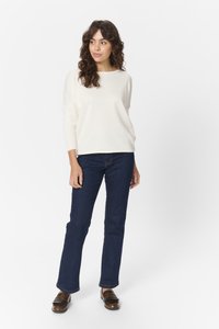 Hvid ribbestrikket sweater med løs pasform og lange ærmer, parret med mørkeblå flared jeans. Brune loafers med frynse detaljer.