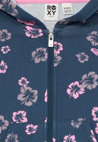 Sweatshirt azul-marinho para meninas com flores de hibisco em rosa e cinza, com fecho de correr frontal completo e etiqueta da marca Roxy dentro da gola.