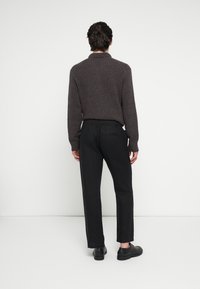 Tamsiai rudas megztinis su apykakle, derinamas su juodomis kelnėmis su elastinga juosmens juosta. Modelis vilki juodus batus, matomas iš nugaros.