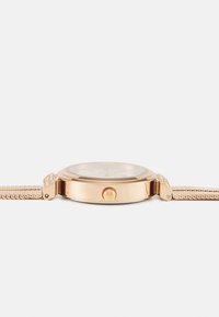 Zlaté náramkové hodinky s okrúhlym puzdrom, sieťovým remienkom a štruktúrovanou korunkou, s priehľadným ciferníkom a decentnými hodinovými značkami.