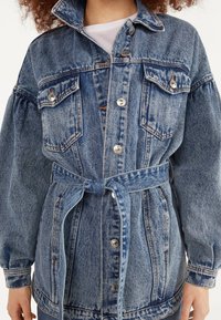 Jeansjacka med bälte, ljusblå tvätt, två bröstfickor, silverfärgad knappar och en lös passform med puffärmar.