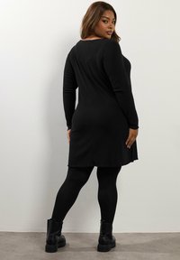 Abito lungo a maniche nere a coste con scollatura rotonda, caratterizzato da un orlo sfrangiato e abbinato a leggings neri e stivali alla caviglia.