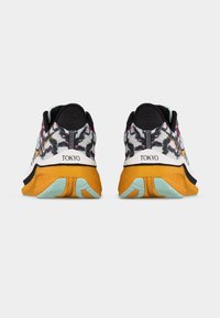 Ζευγάρι πολύχρωμα αθλητικά παπούτσια με πορτοκαλί σόλες, επάνω μέρος με ασπρόμαυρο σχέδιο και την επιγραφή «TOKYO» στις φτέρνες.