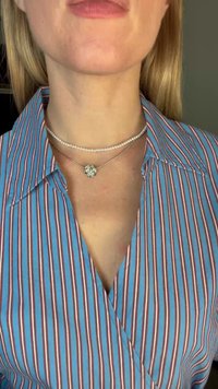 Drei geschichtete Halsketten: eine Perlenkette, eine Silberkette mit einem runden Anhänger und eine kurze metallische Kette. Die Trägerin trägt ein gestreiftes Shirt in Blau und Rot.