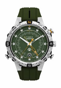 Hodinky Timex Expedition s zeleným gumovým remienkom, strieborným puzdrom, tmavozeleným ciferníkom, oranžovými akcentmi, kompasom a ukazovateľmi prílivu. Odolný dizajn.