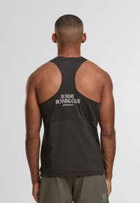 Canotta atletica nera con ampie aperture per le braccia, con un design a schiena aperta e il testo "SUNDAY RUNNING CLUB" in bianco. Tessuto liscio.