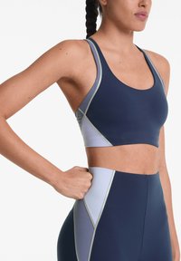 Marine sportbeha met lichtgrijze accenten, racerback ontwerp en een gladde textuur. Bevat contrasterende naden en een aansluitende pasvorm.