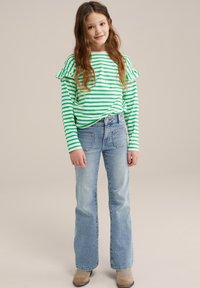 Grön och vit randig långärmad skjorta med volangdetaljer, paired med ljusblå utsvängda jeans och beige ankellånga stövlar.