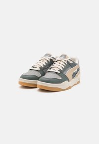 Chaussures de sport vertes et beiges en cuir et en caoutchouc, présentant un design à lacets, une boîte à orteils perforée et une semelle en caoutchouc avec des accents en gomme.
