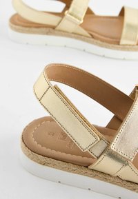 Metallist kuldsed sandaalid, millel on laia rihma disain, tekstureeritud pind ja pehmendatud sisetald, valge kummitald ja espadrille detailid.