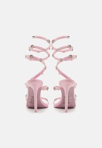 Pink high-heeled sandals with shimmering straps, heart-shaped embellishments, and a glossy finish. Features a sleek stiletto design.