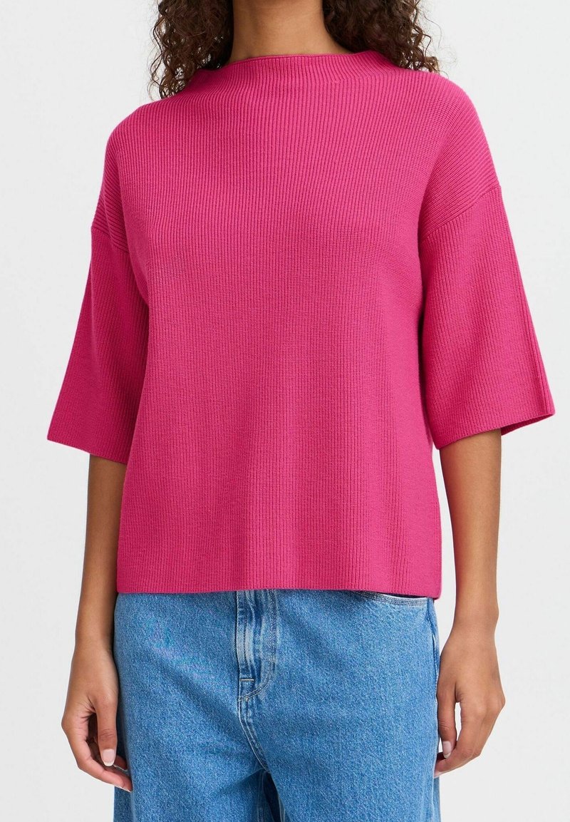 Haut court à manches courtes côtelé rose avec un col montant, une coupe décontractée et un tissu texturé. Assorti à un jean en denim bleu.