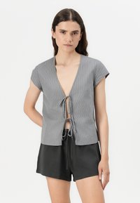 Gray striped top with short sleeves, deep V-neck, and front tie closure. Paired with black shorts, minimalist design and lightweight fabric.