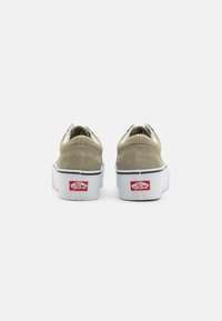 Zapatillas de ante beige con suela de goma blanca, que cuentan con un collar acolchado, acentos cosidos y un logo rojo de Vans en el talón.