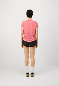 Kortärmad rosa träningsskjorta, mjukt tyg, avslappnad passform, tillsammans med svarta shorts och vita sportstrumpor, sedd bakifrån.