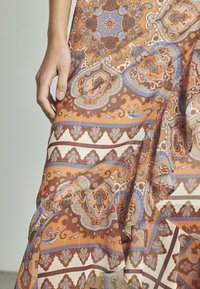 Tissu à motifs dans des tons chauds d'orange et de marron, présentant des dessins détaillés de paisleys et de formes géométriques avec des accents bleus.