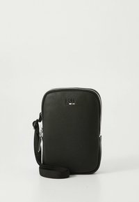 Liten svart teksturert lær crossbody-veske med en sølvglidelås og justerbar vevd stropp på hvit bakgrunn.