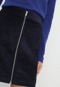 Jupe en velours côtelé bleu marine au design ajusté, dotée d'une fermeture éclair argentée sur le devant et d'une texture de ceinture lisse.