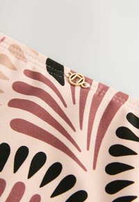 Mönstrad tyg i pastellnyanser av rosa, vinröd och svart; har en dekorativ guldaccent med en cirkulär design nära sömmen.