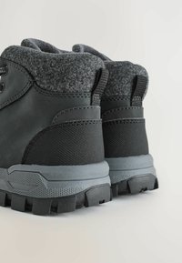 Bottes de randonnée noires avec un col en feutre gris, semelle en caoutchouc texturée et œillets renforcés. Elles sont dotées d'une languette au talon pour un enfilage facile.